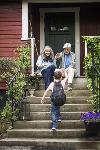 Rear view of boy waving at grandparents sitting on front stoop