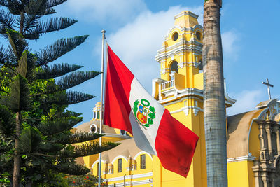 Low angle view of peruvian flag against yellow historic building against sky