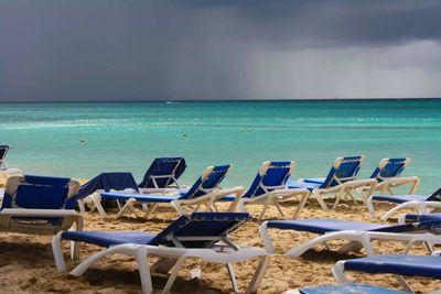 Deck chairs at beach against cloudy sky