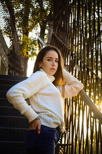 Portrait of young woman standing against railing