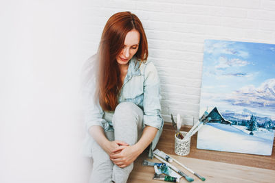 Woman sitting against wall at home