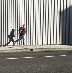 Young businessman running on pavement along building