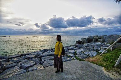 Woman standing on rock by sea against sky