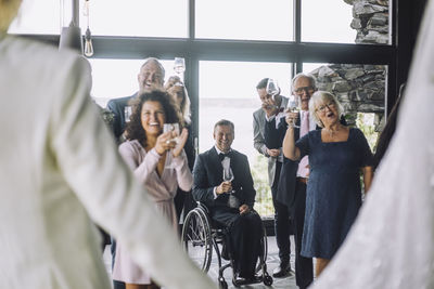 Happy multiracial guests with wineglasses cheering newlywed couple at wedding ceremony