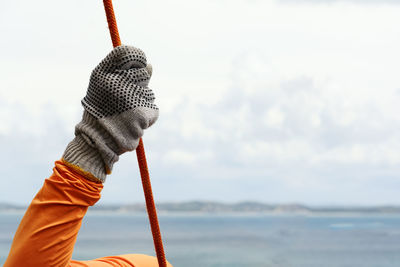 Close-up of hand with glove holding a rope against the sky.