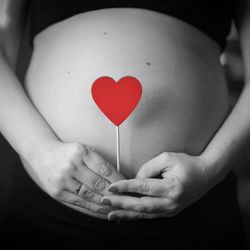 Midsection of pregnant woman holding heart shape at home
