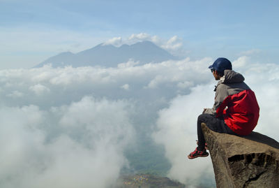 Hiker sitting on rock at mountain against cloudscape