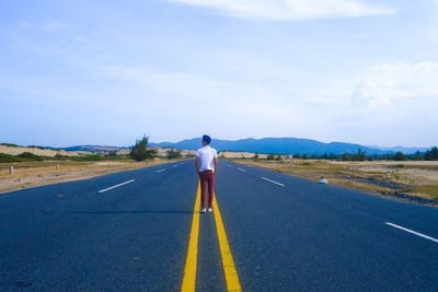 Rear view of man standing on country road against sky