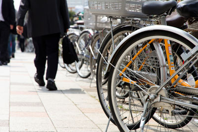 Low section of businessman walking on footpath by bicycles