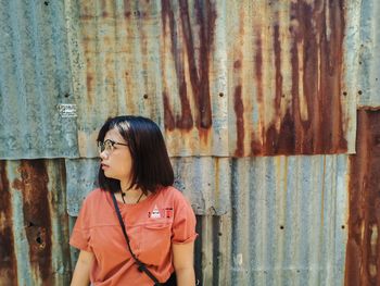 Young woman looking away while standing against corrugated iron