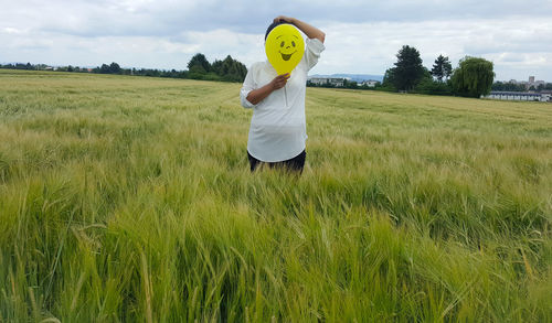 Person holding balloon with smiley over face while standing on field