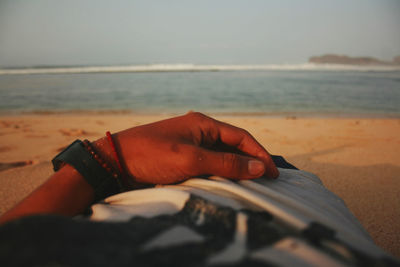 Midsection of person hand on sand at beach against sky