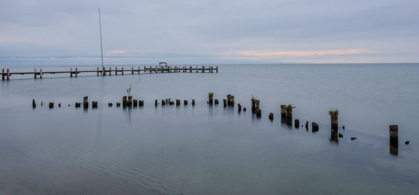 Wooden posts in sea against sky during sunset