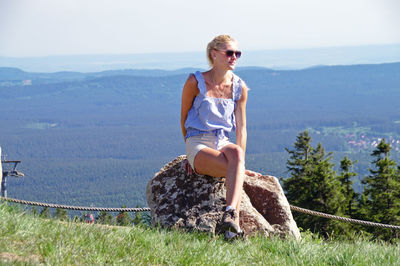 Full length of woman sitting on rock against landscape