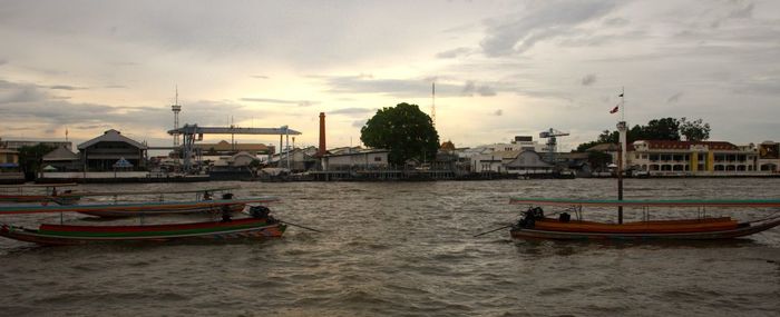 Sailboats moored on sea against buildings in city at sunset