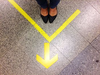 Low section of woman wearing shoes standing by arrow sign on tiled floor