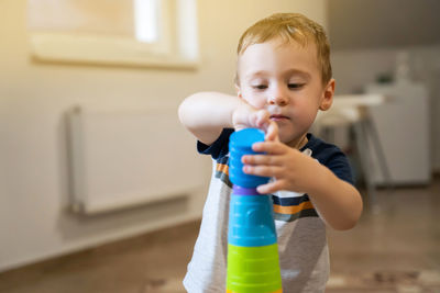 A cute little boy is playing with a multi-colored pyramid indoors. 