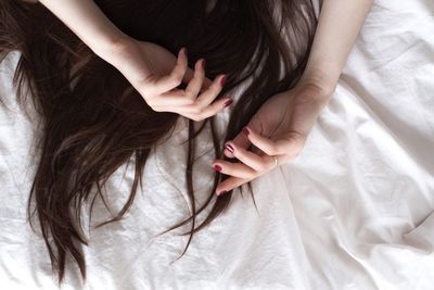 Cropped hands of woman with long hair on bed at home