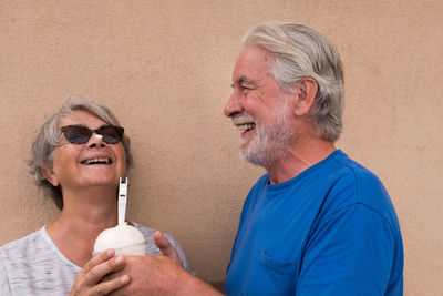 Smiling senior couple holding drink against wall