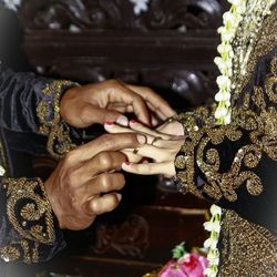 Midsection of bridegroom putting ring on woman finger in wedding ceremony