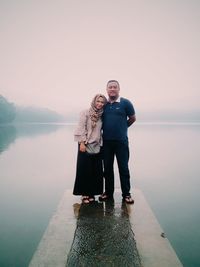 Young couple standing by lake against clear sky