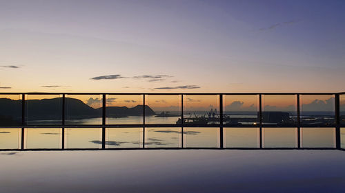Silhouette swimming pool by lake against sky during sunset
