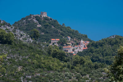 Trees and houses on mountain against clear sky