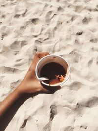 Low section of woman holding coffee cup at beach