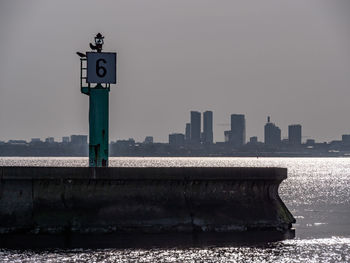 Information sign by sea against buildings in city against clear sky