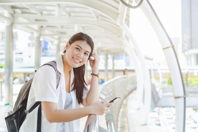 Portrait of young woman using mobile phone while standing by railing