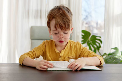 Kid sitting on chair reading a book, wearing glasses