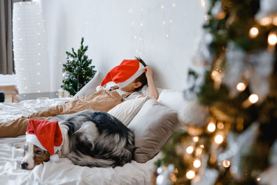 A boy and a dog in red santa hat laying on the bed. best friends. christmas mood. festive atmosphere