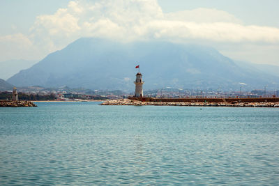 Lighthouse amidst buildings and mountains against sky