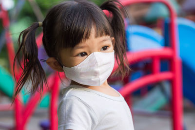 
cute girl wearing mask looking away while standing outdoors