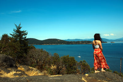 Rear view of woman standing by sea against blue sky