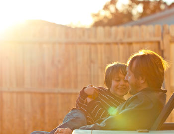 Father and son sitting on chair in backyard