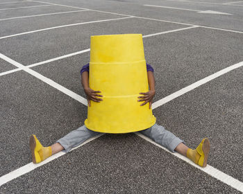 High angle view of man holding yellow container while sitting on road