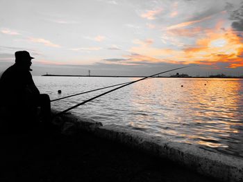 Silhouette man fishing by sea against sky during sunset