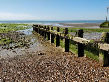 Wooden posts on beach by sea against sky