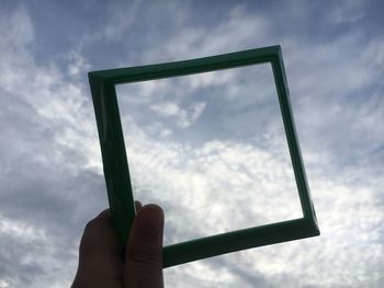 Cropped hand holding picture frame against sky 