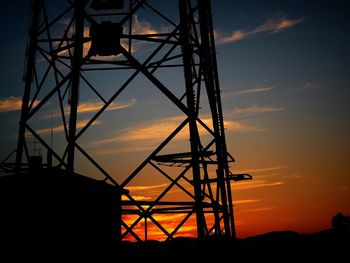 Low angle view of silhouette cranes against orange sky