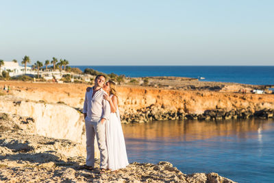 Couple standing on beach by sea against sky