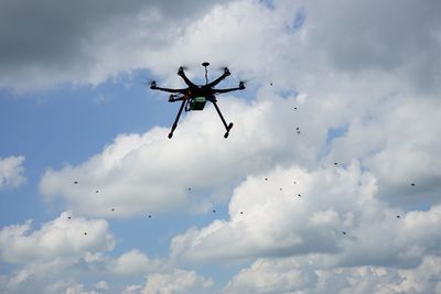 Low angle view of drone flying against cloudy sky