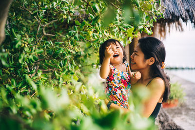 Smiling mother and daughter by tree