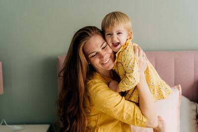 Happy freckled mother cuddling her daughter in the bedroom in the morning.