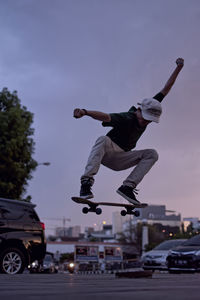 Full length of man jumping with skateboard on street against sky