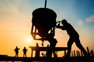 Silhouette construction worker pouring concrete on site against sky during sunset