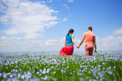 Rear view of couple walking on field against sky