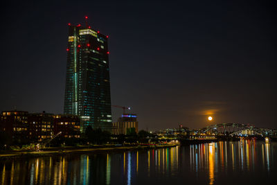 Illuminated buildings by river against sky at night