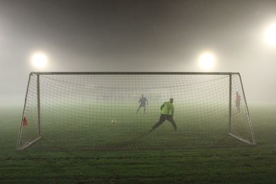 People playing soccer ball on grass against sky